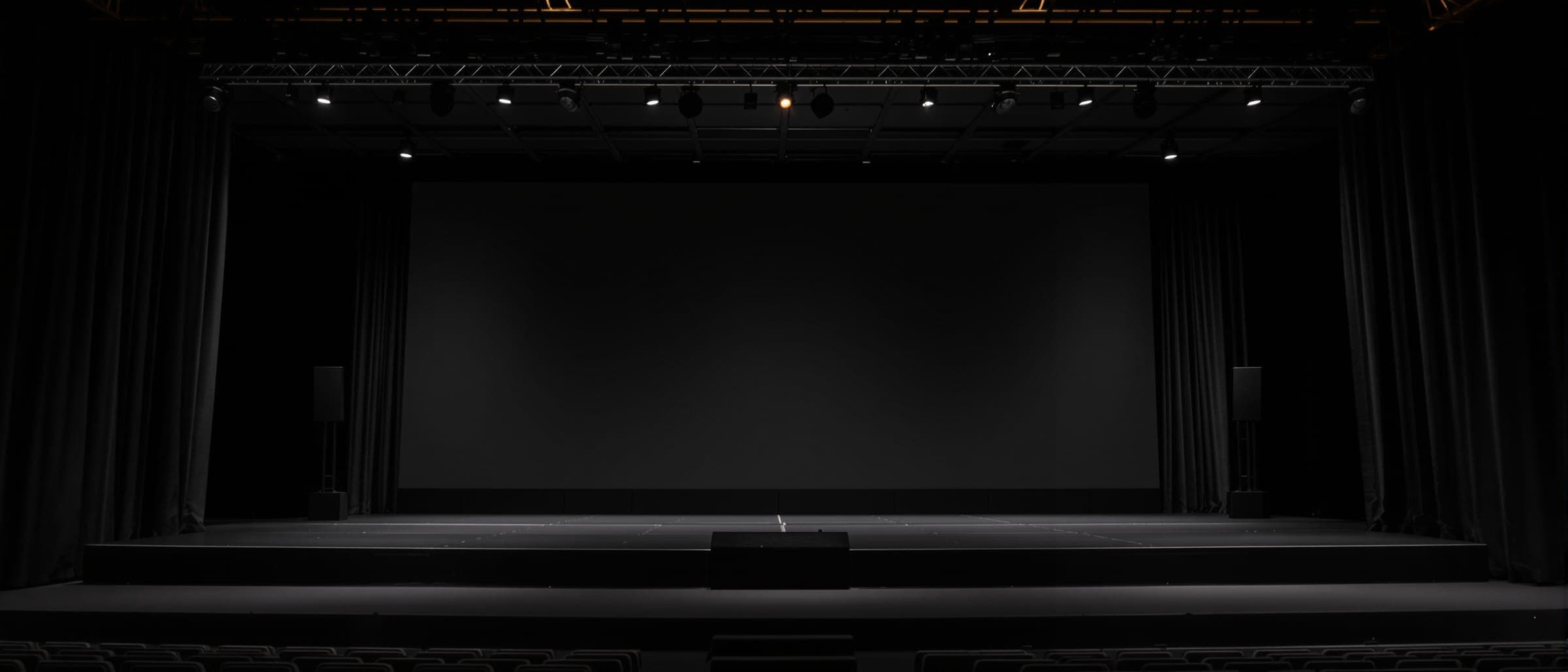 An empty stage in a dark hall, lit softly before an event.