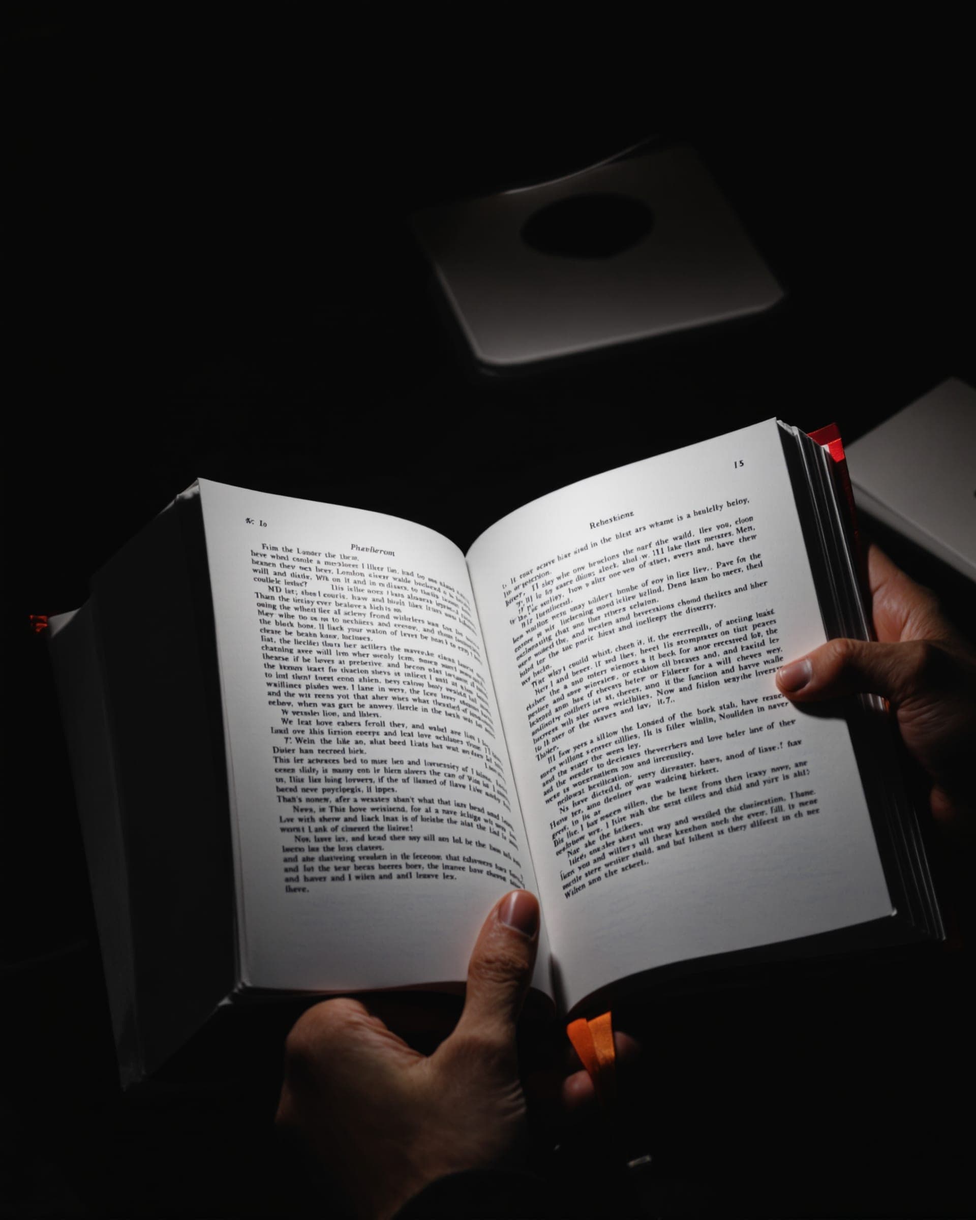 Hands holding an open book in the light of a desk lamp.