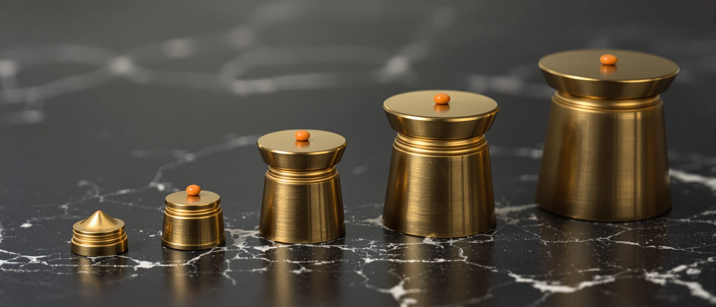 A row of brass weights increasing in size on dark marble.