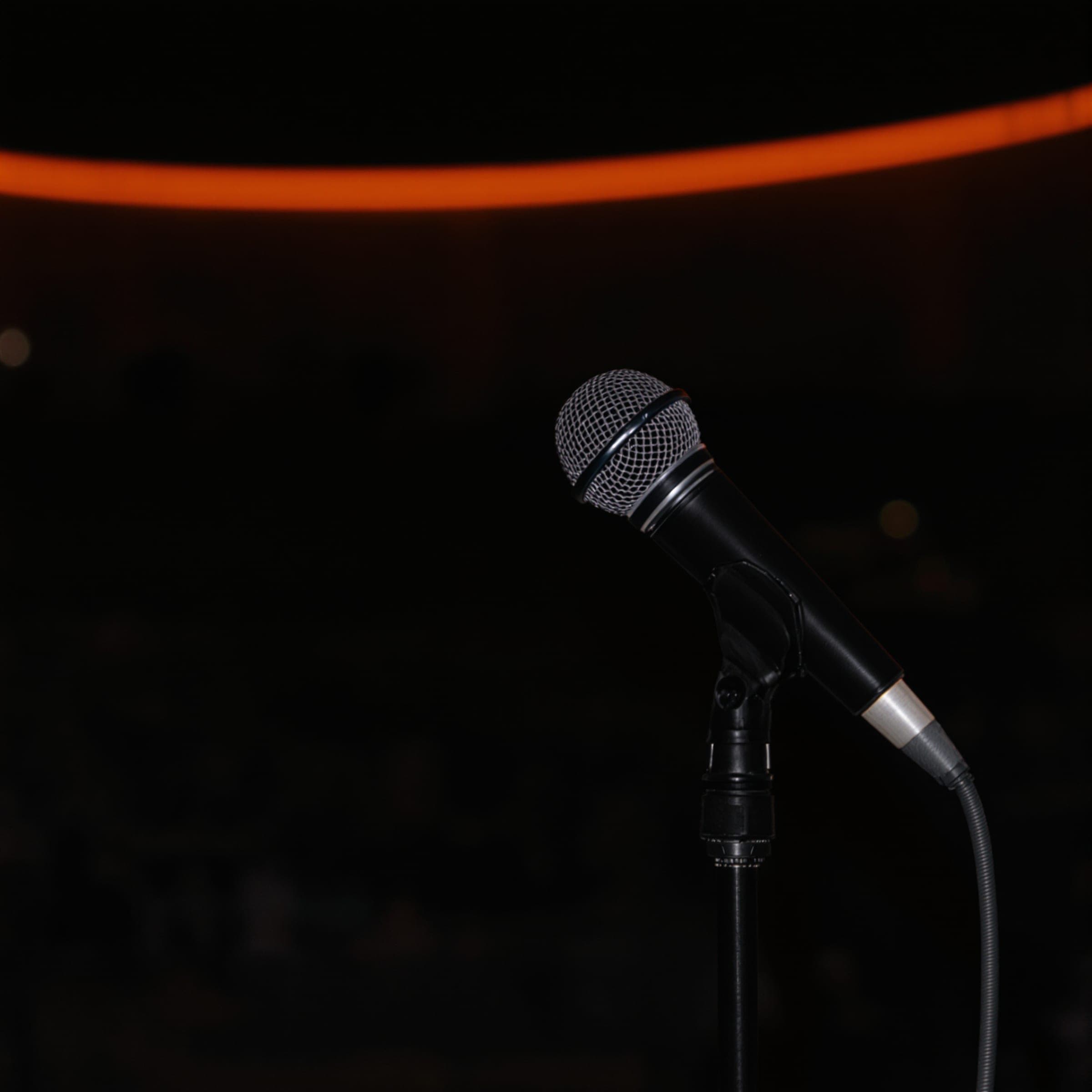 A microphone on a stand in a dark venue under a thin orange light.