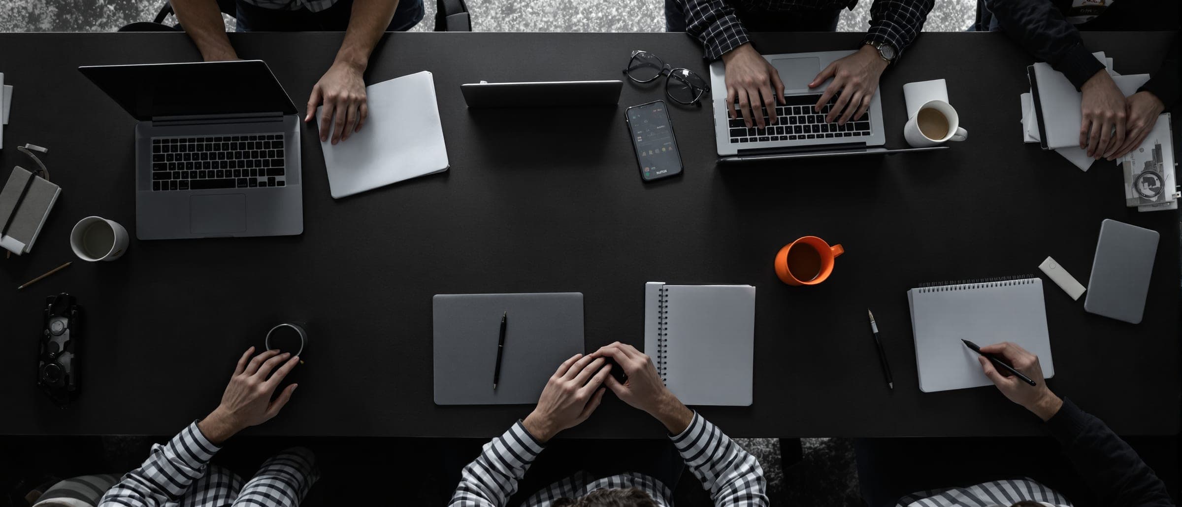 A small team working at laptops around a long dark table, seen from above.
