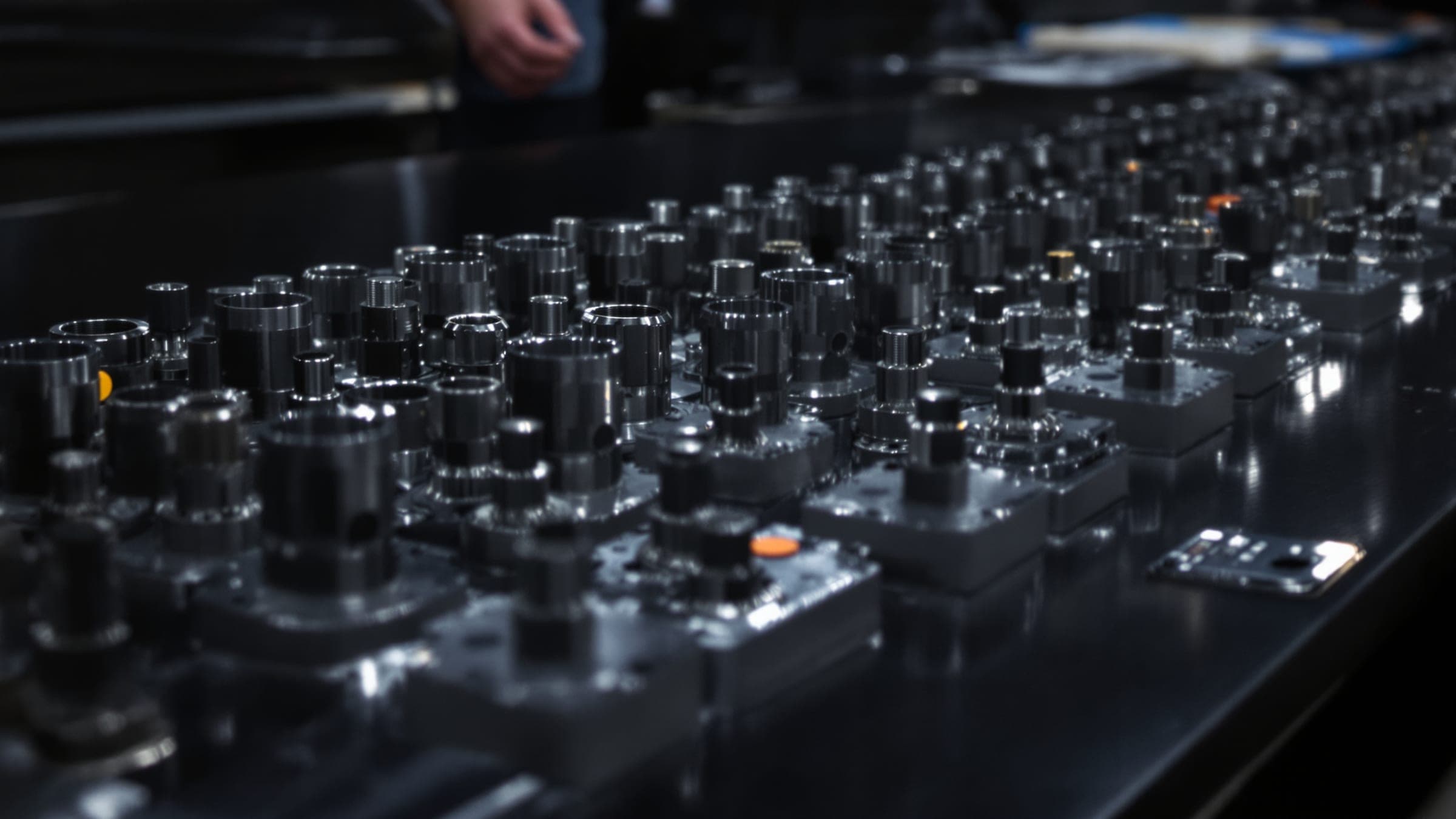 Rows of identical machined steel parts on a dark bench.