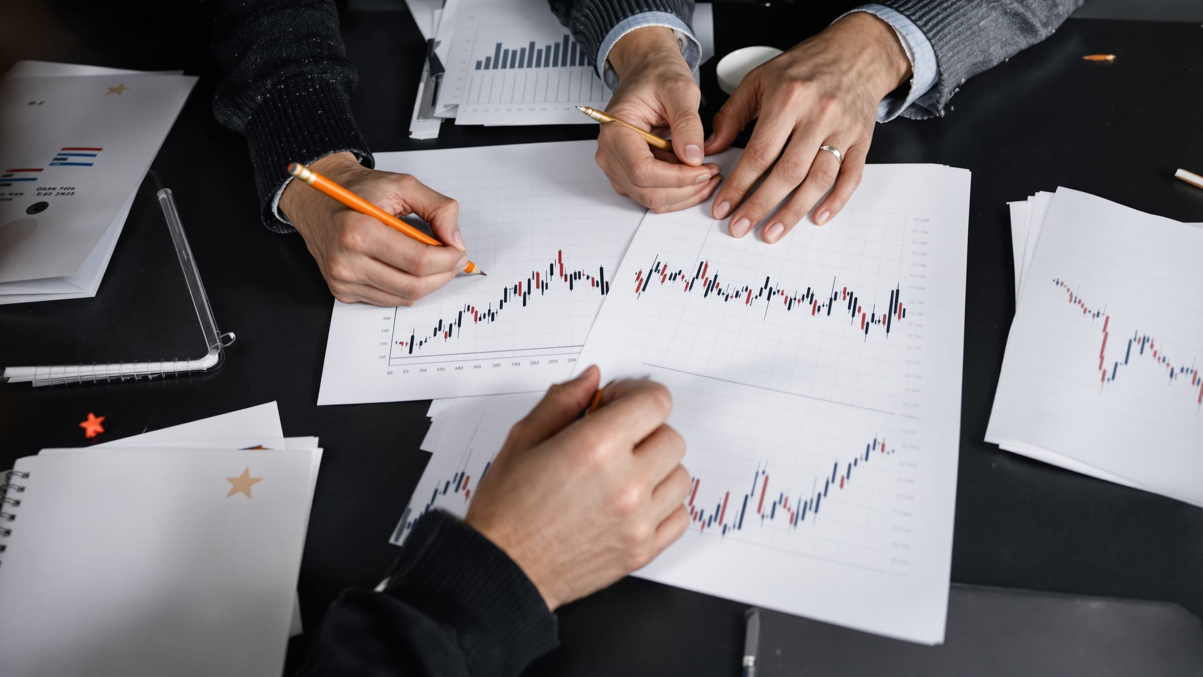 Two people marking printed charts with pencils, seen from above.