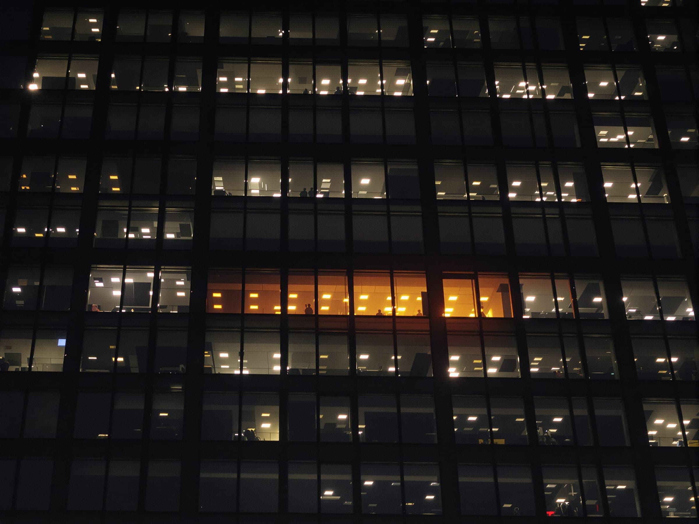 The lit windows of an office tower at night, one row glowing orange.