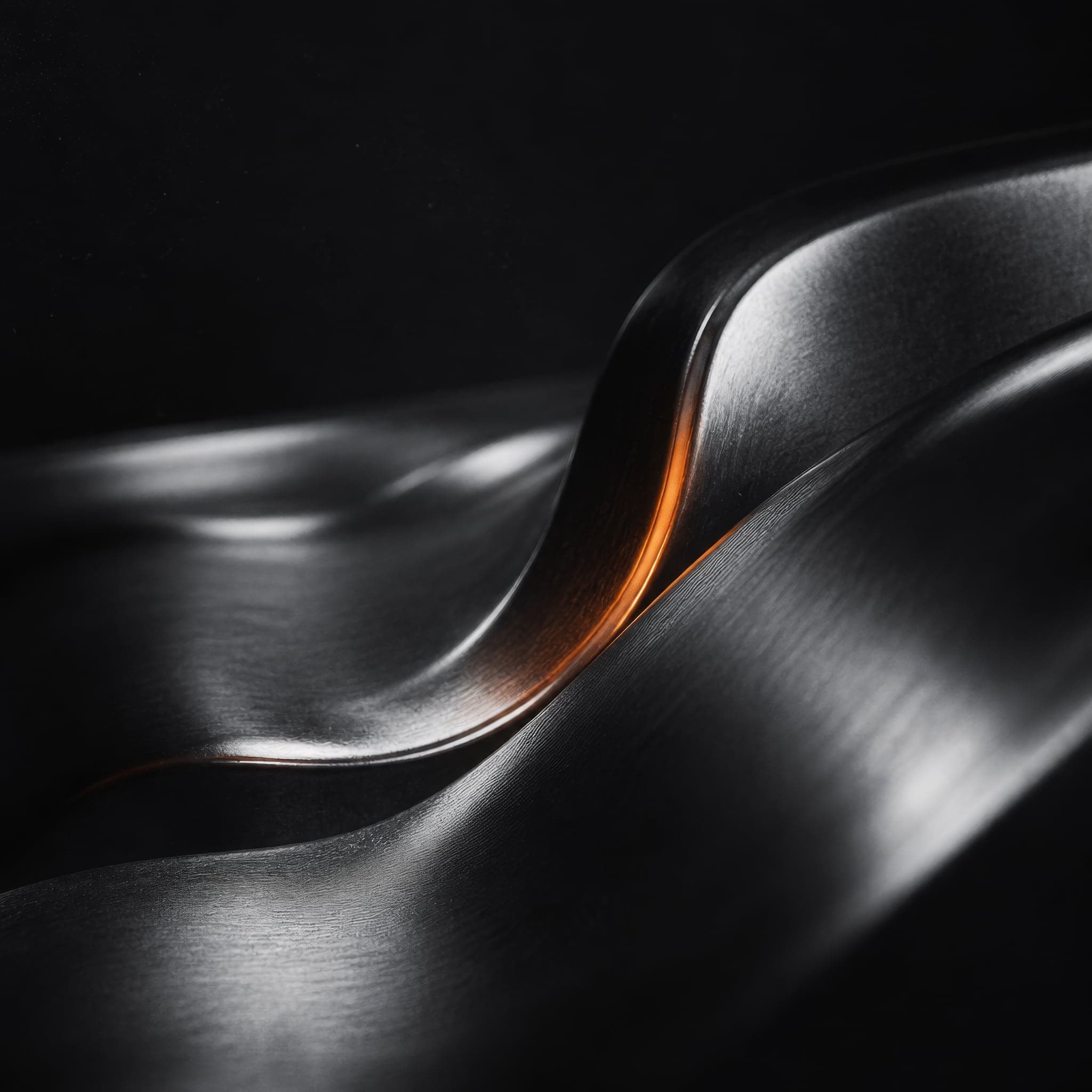 A close-up of curved, brushed dark metal with silver reflections and a thin orange edge.