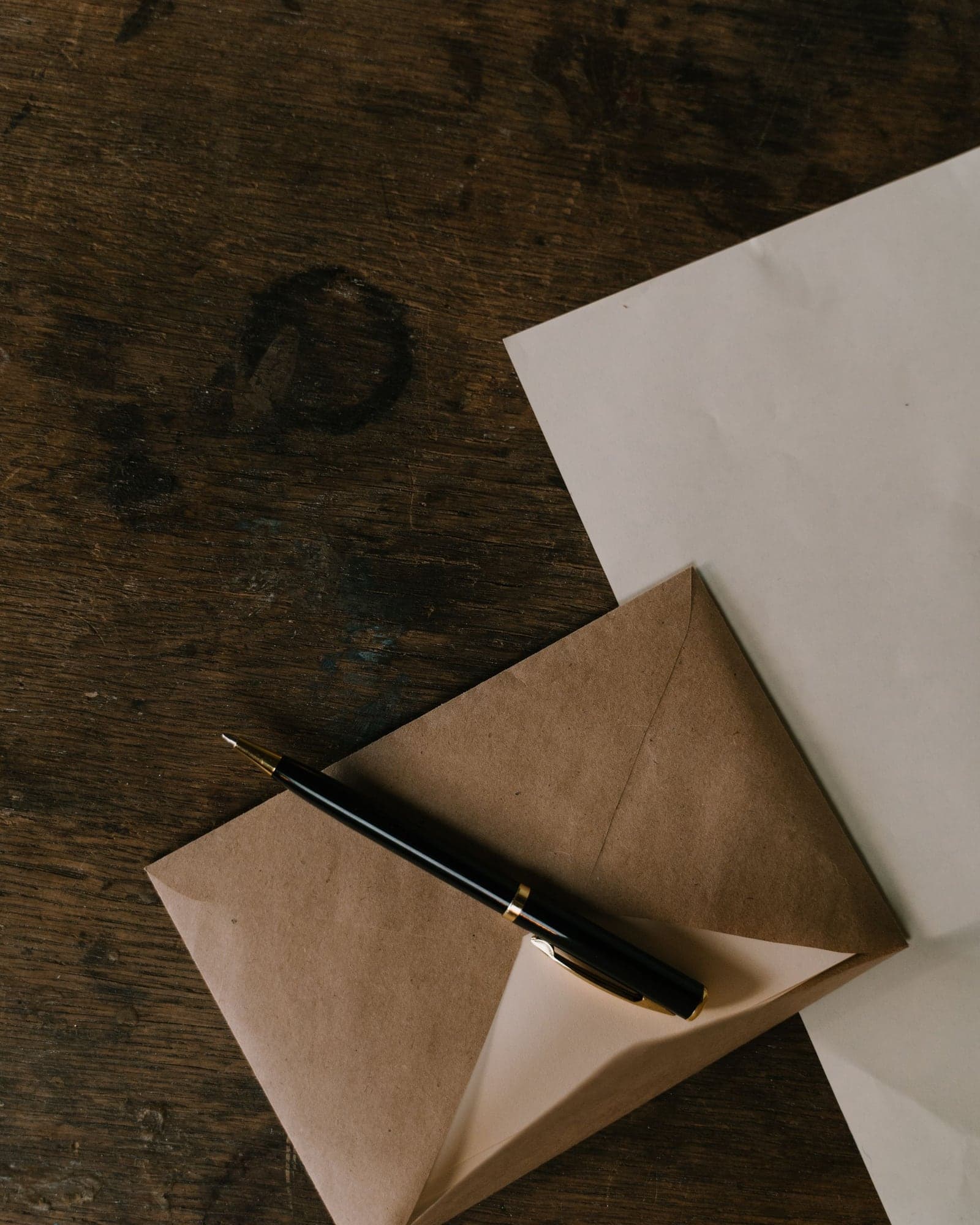 A black pen resting on a brown paper envelope on a dark wooden desk.