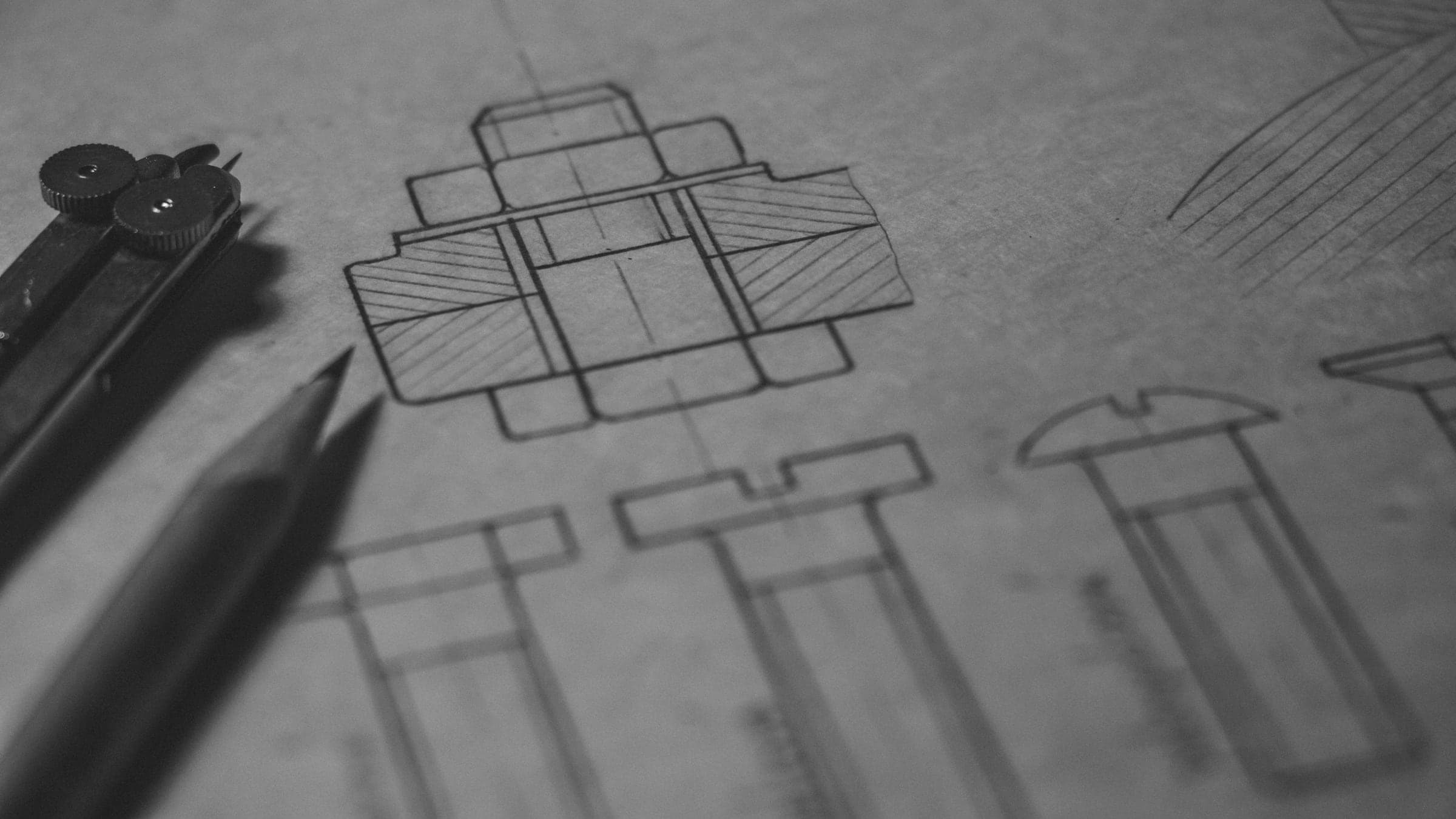 A pencil and a pair of dividers resting on a technical drawing of bolts and nuts.