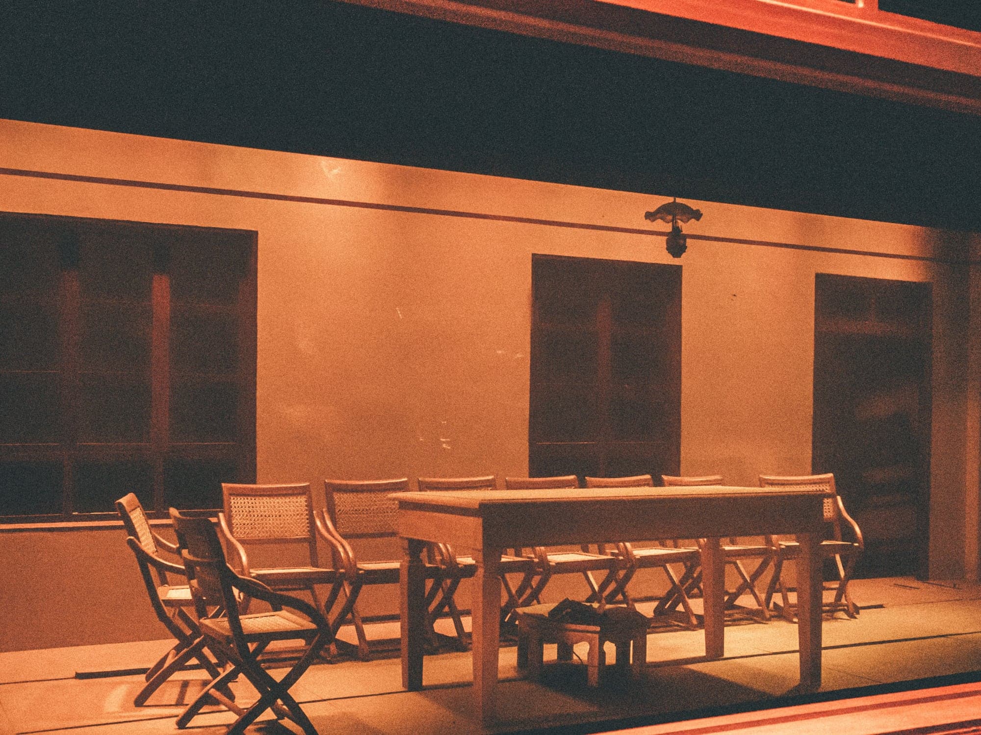 An empty wooden table and folding chairs under warm orange light at night.