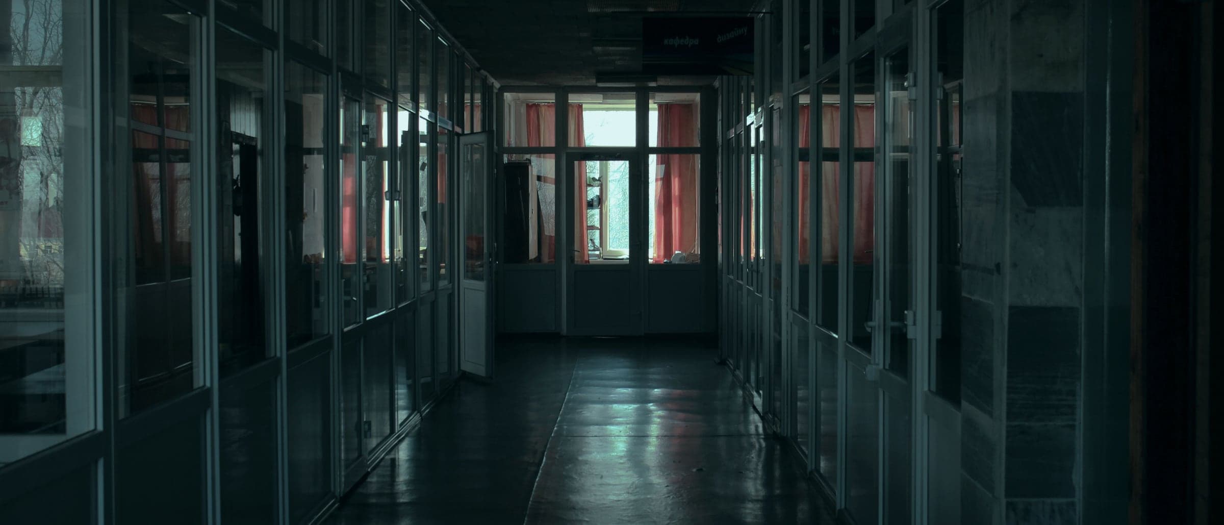 A long, dim corridor lined with glass doors, cool light falling across the floor.
