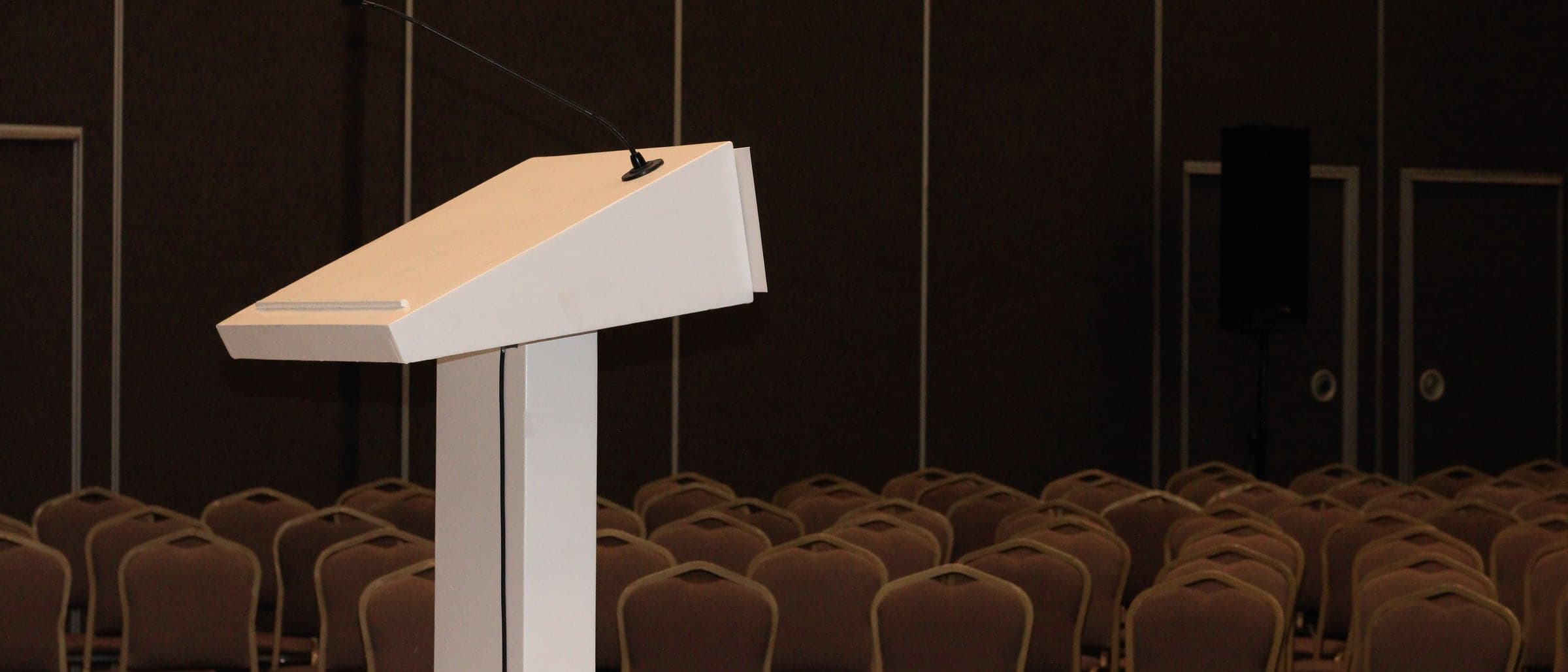 A white lectern at the front of a hall set out with rows of empty chairs.