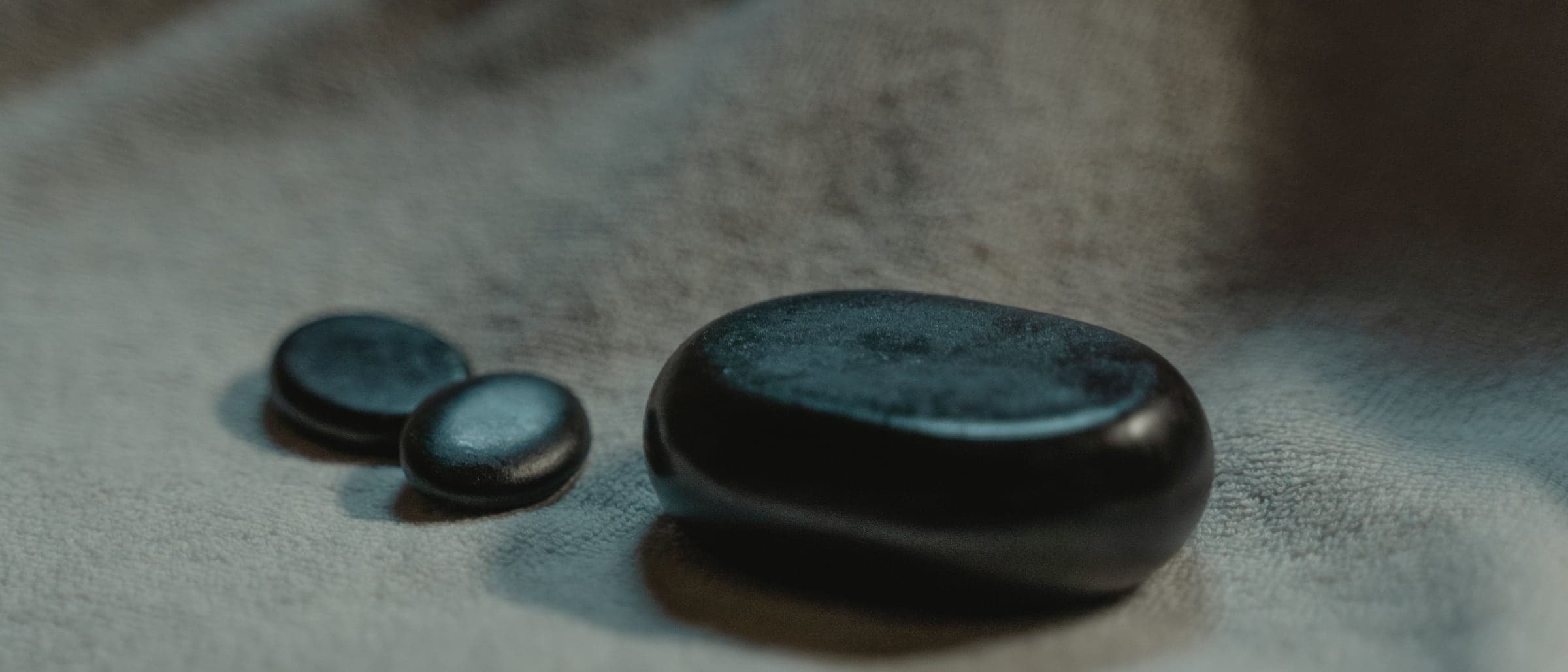 Three smooth black stones of different sizes resting on soft grey cloth.