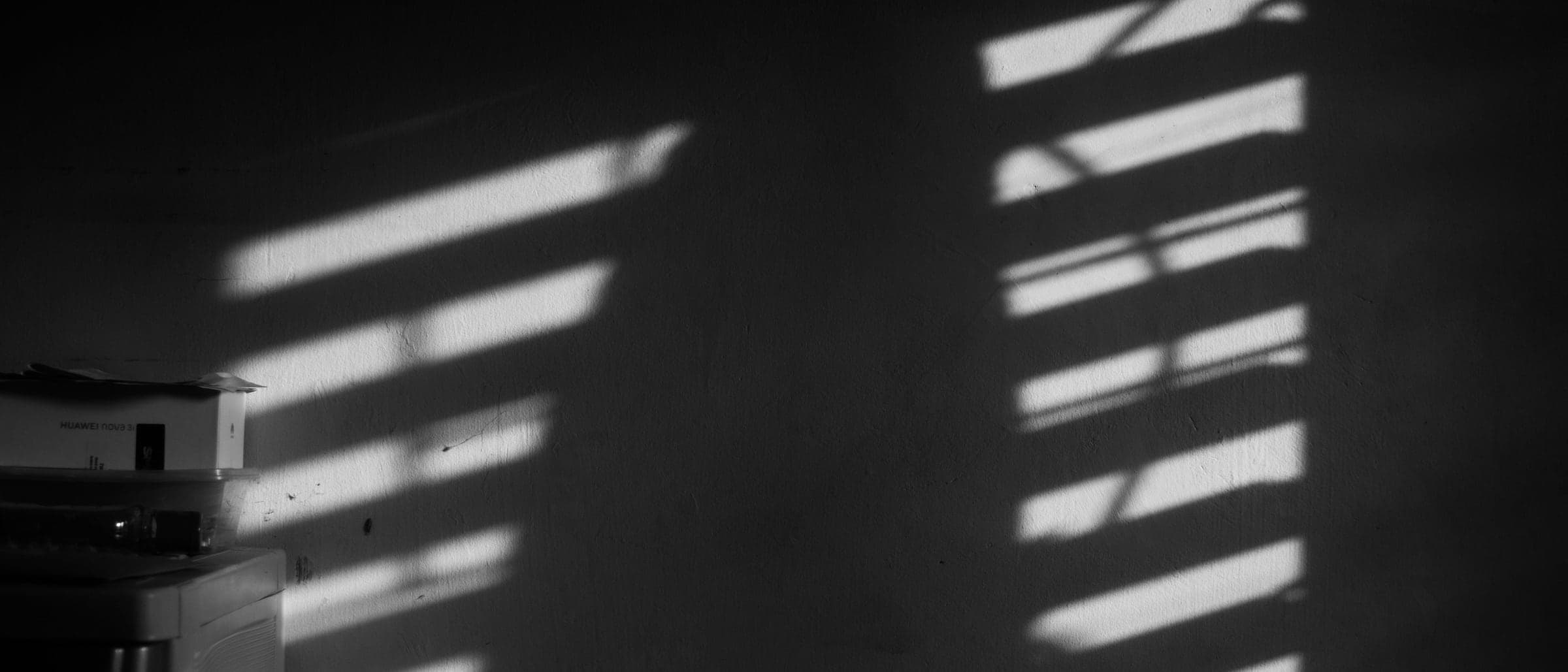 Stripes of light from window blinds falling across a dark wall.