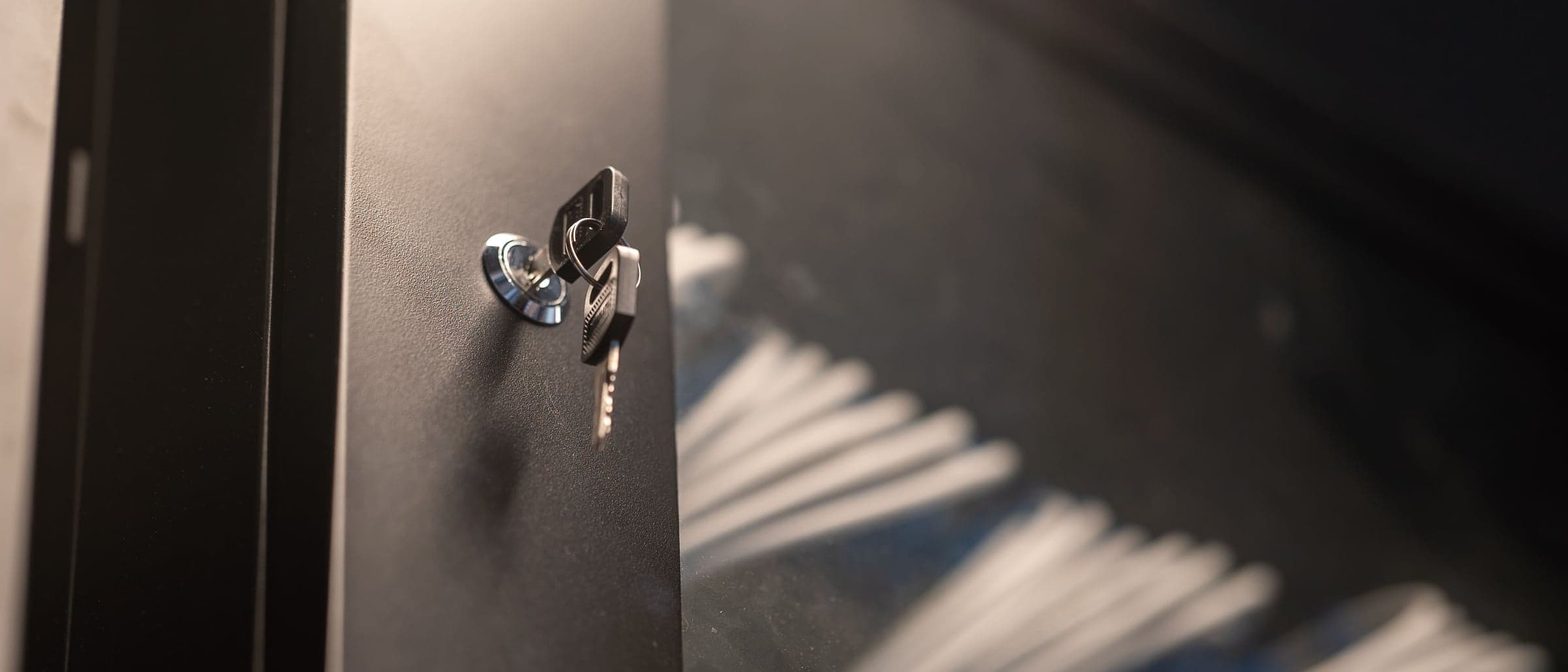 A key left in the lock of a dark metal cabinet, light falling in stripes beside it.