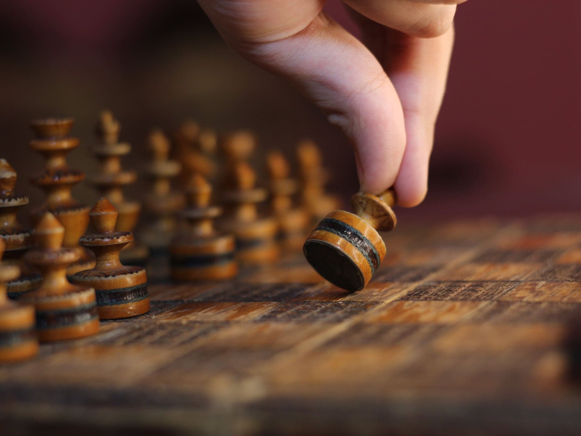 A hand moving a wooden chess piece across a board in warm light.