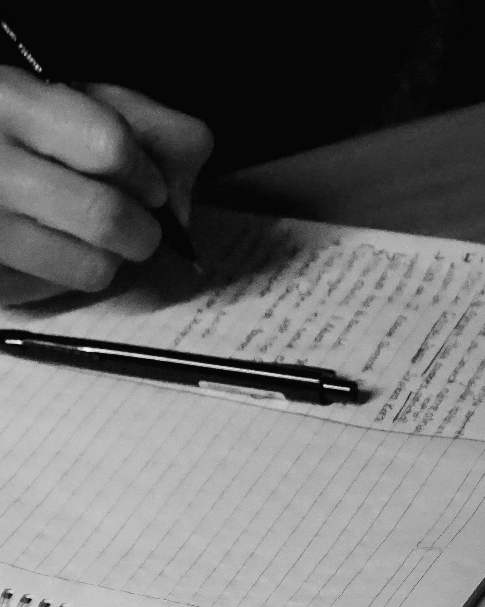 A hand writing notes in a lined notebook, a pen resting across the page, face not shown.