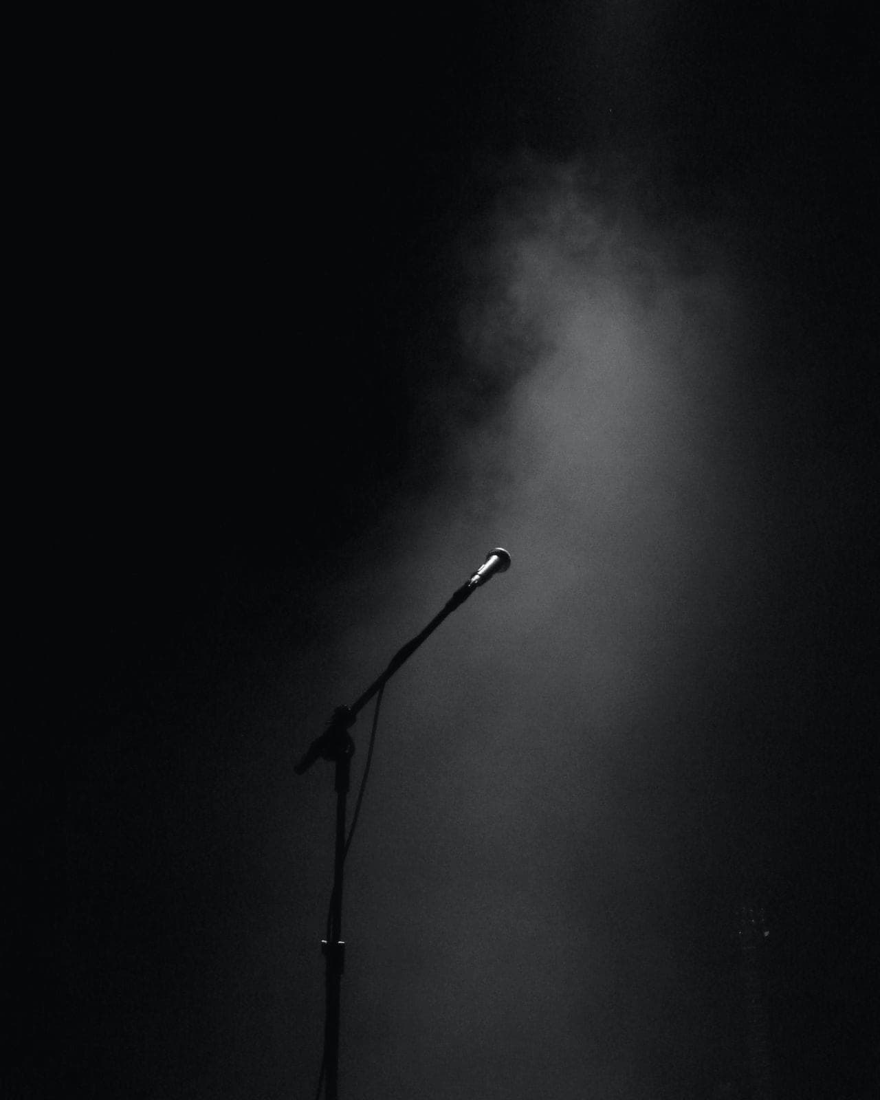 A microphone stand on a dimly lit, empty stage with atmospheric haze.