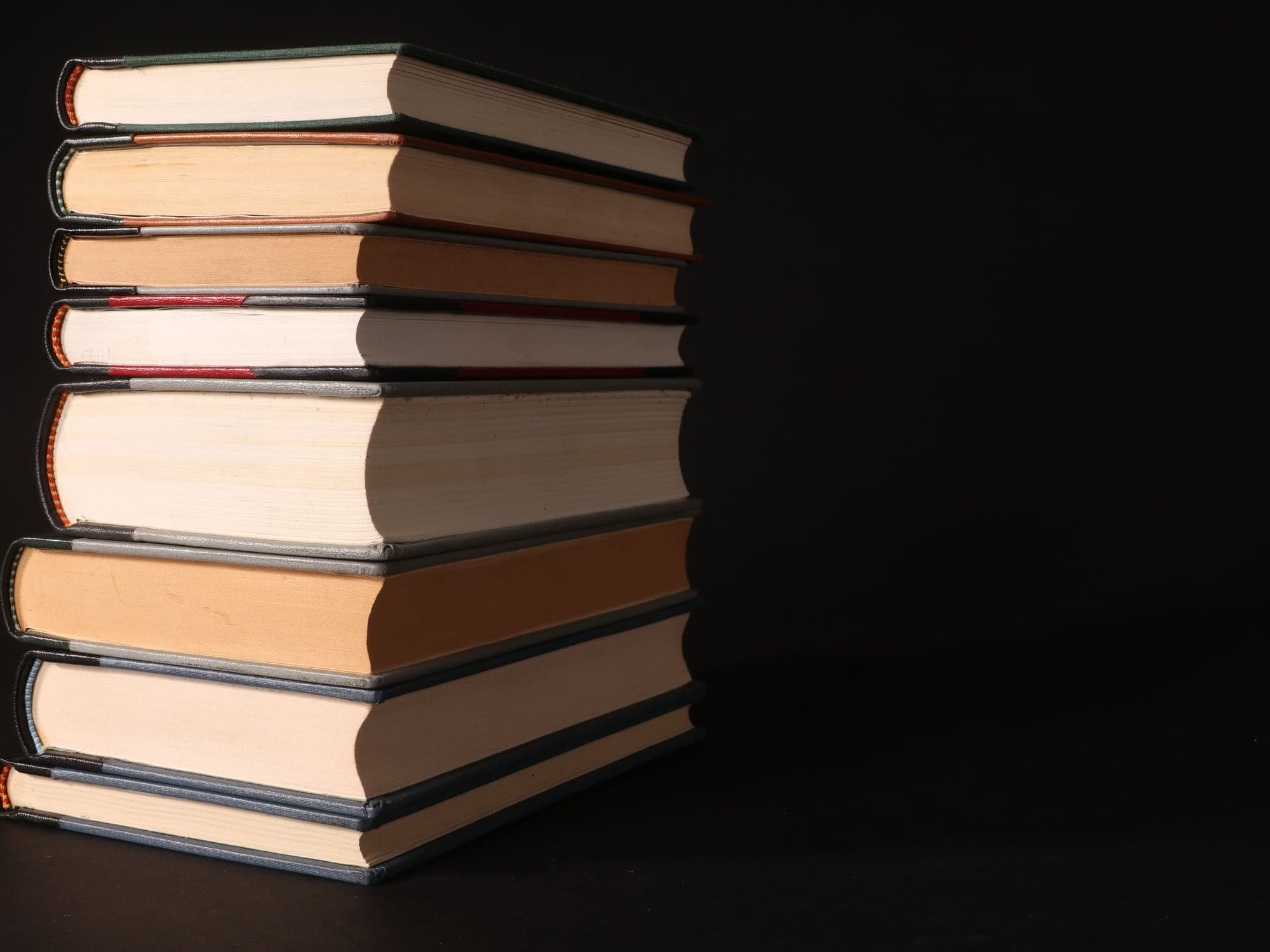 A tall stack of hardback books on a dark surface.