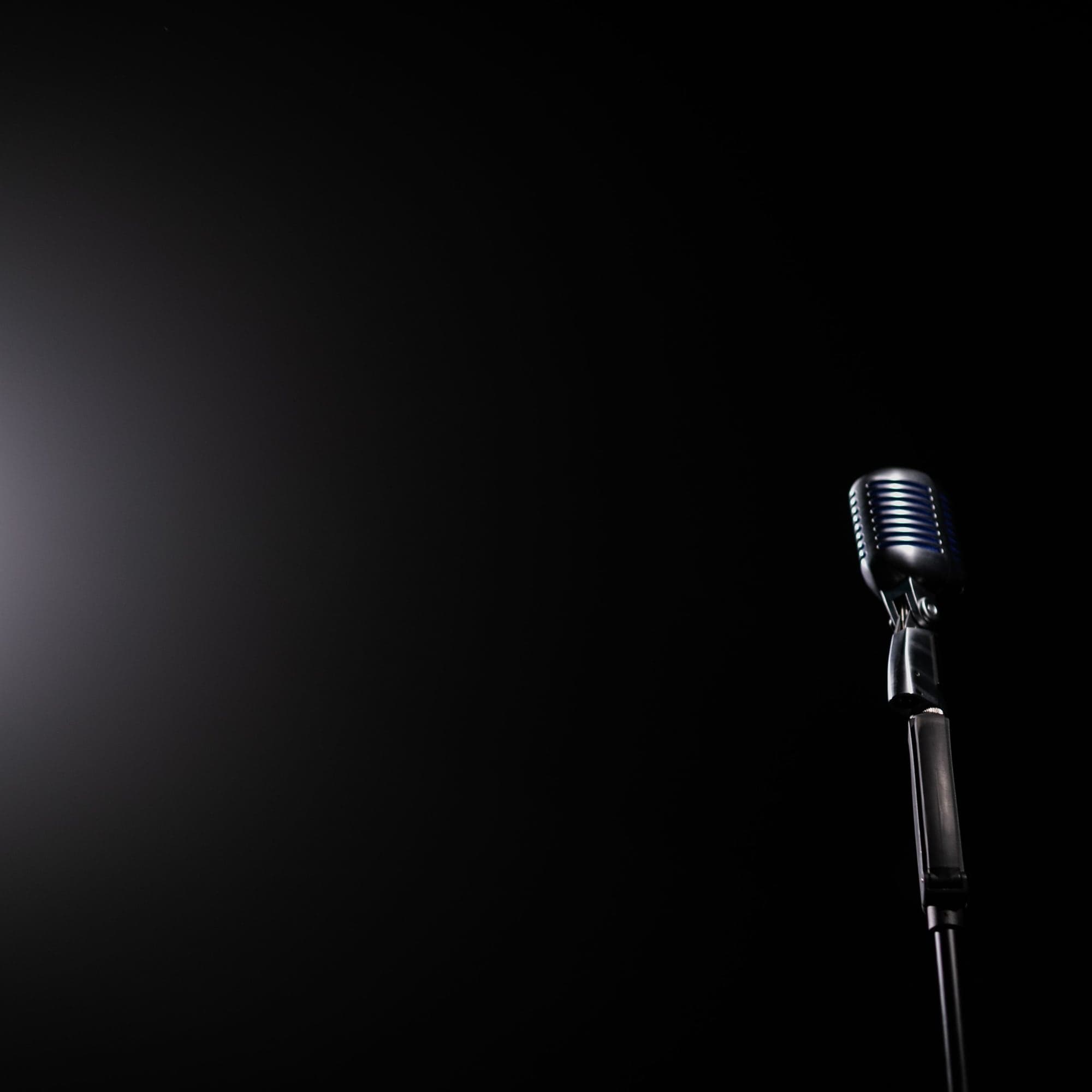 A vintage microphone on a stand in a dark room, lit from one side.