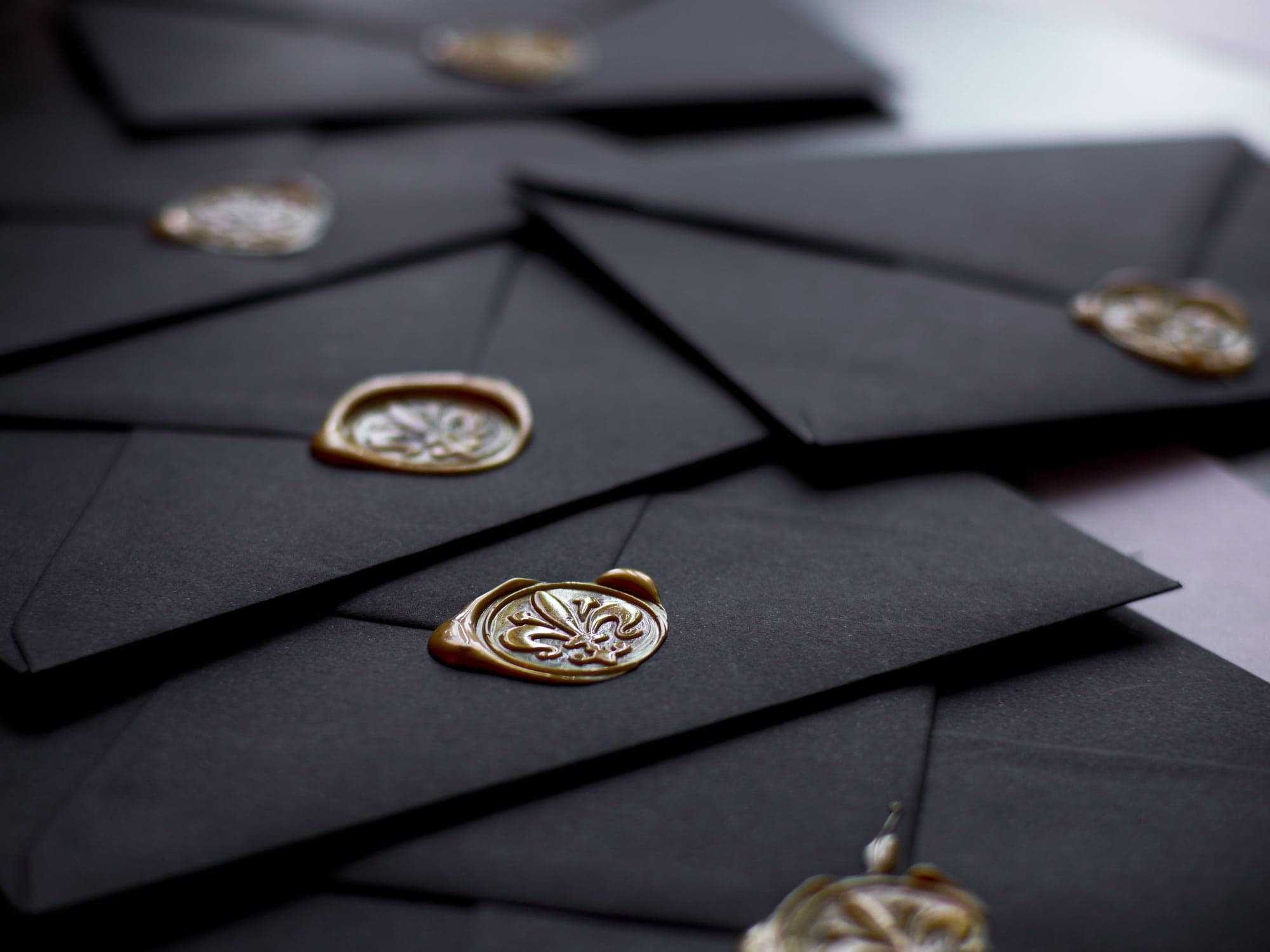 Black envelopes sealed with gold wax, scattered across a dark surface.
