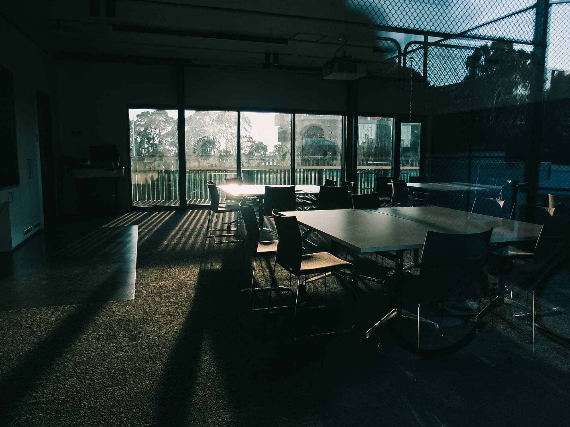 An empty meeting room with long tables and chairs, low sun casting shadows across the floor.