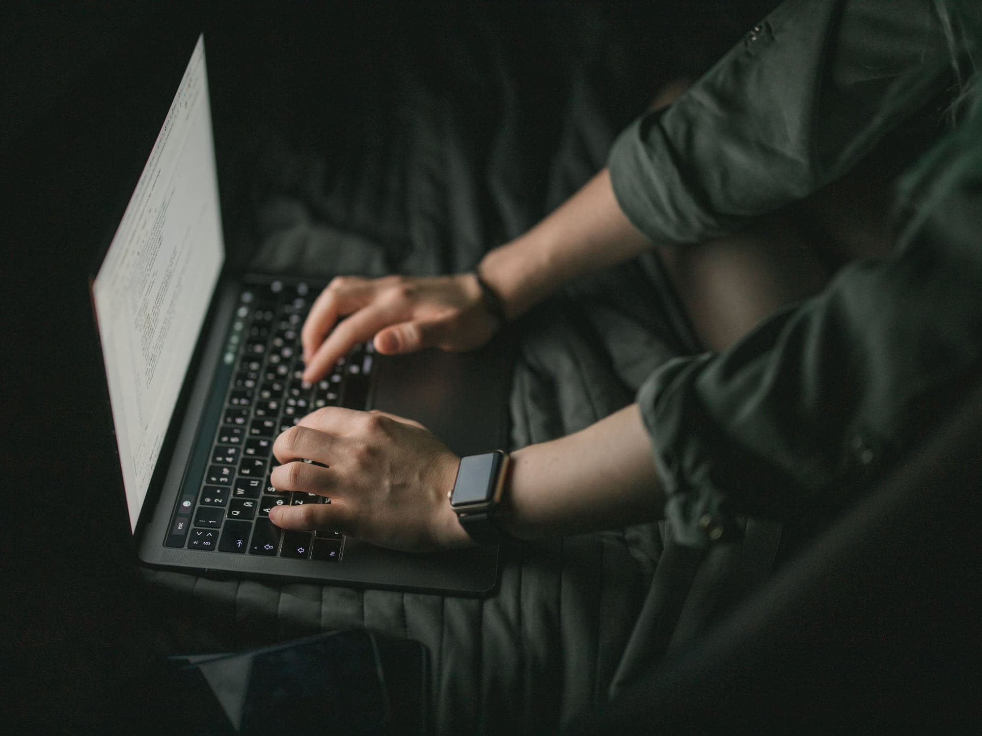 Hands typing on a laptop in a dark room, the screen glowing softly.