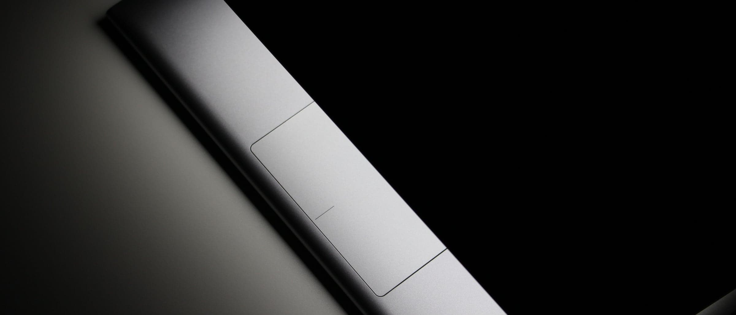 The edge of a closed silver laptop catching light against a black background.
