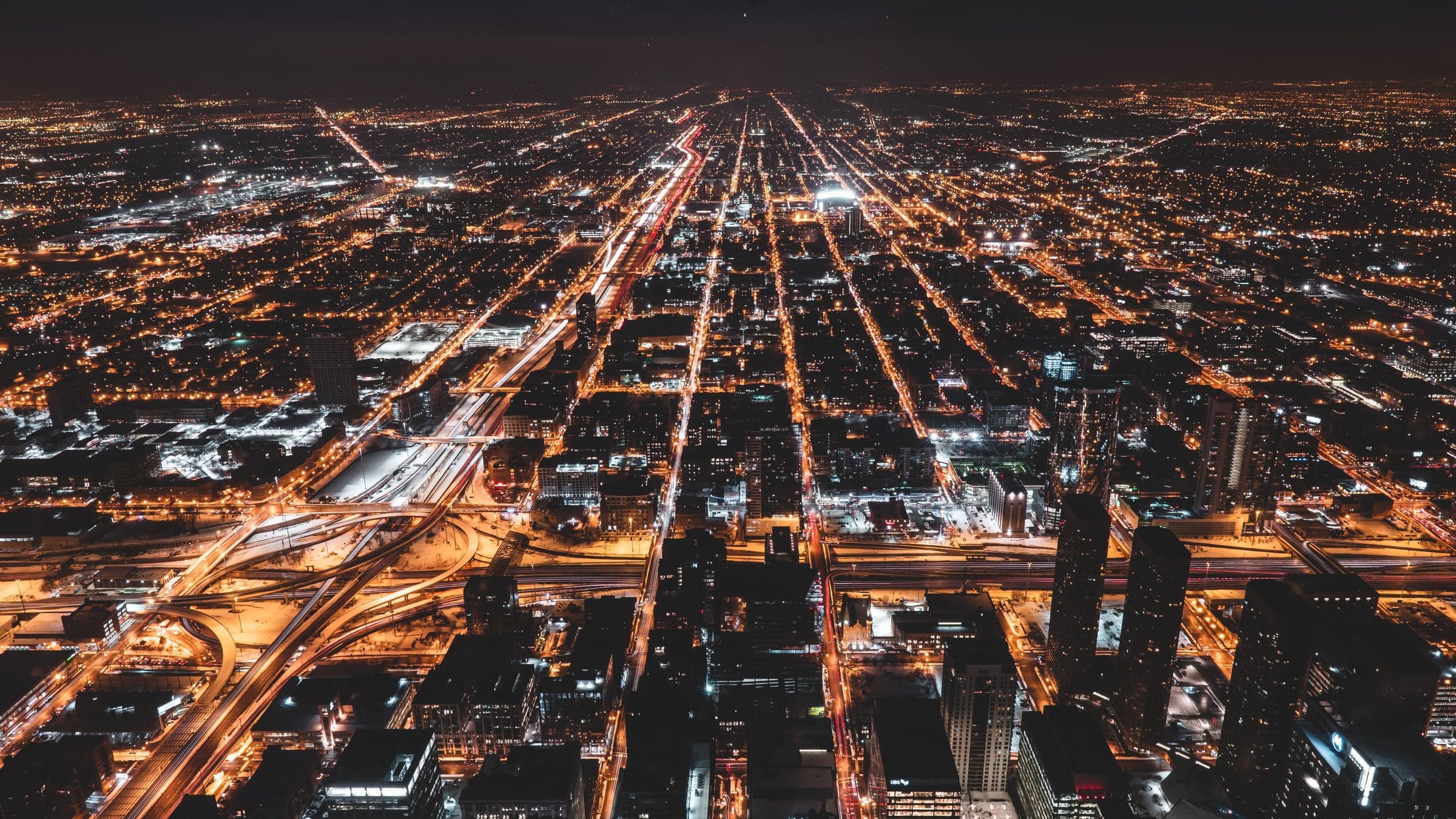 A city at night seen from high above, its streets glowing in a dense grid of lights.