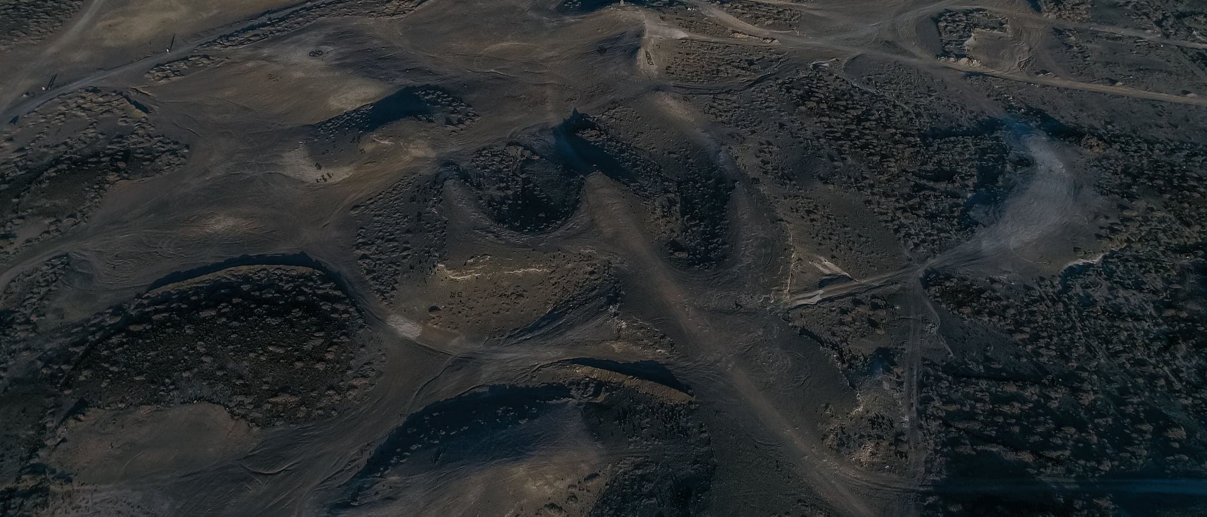 An aerial view of dark, rolling terrain with ridges and valleys in soft light.