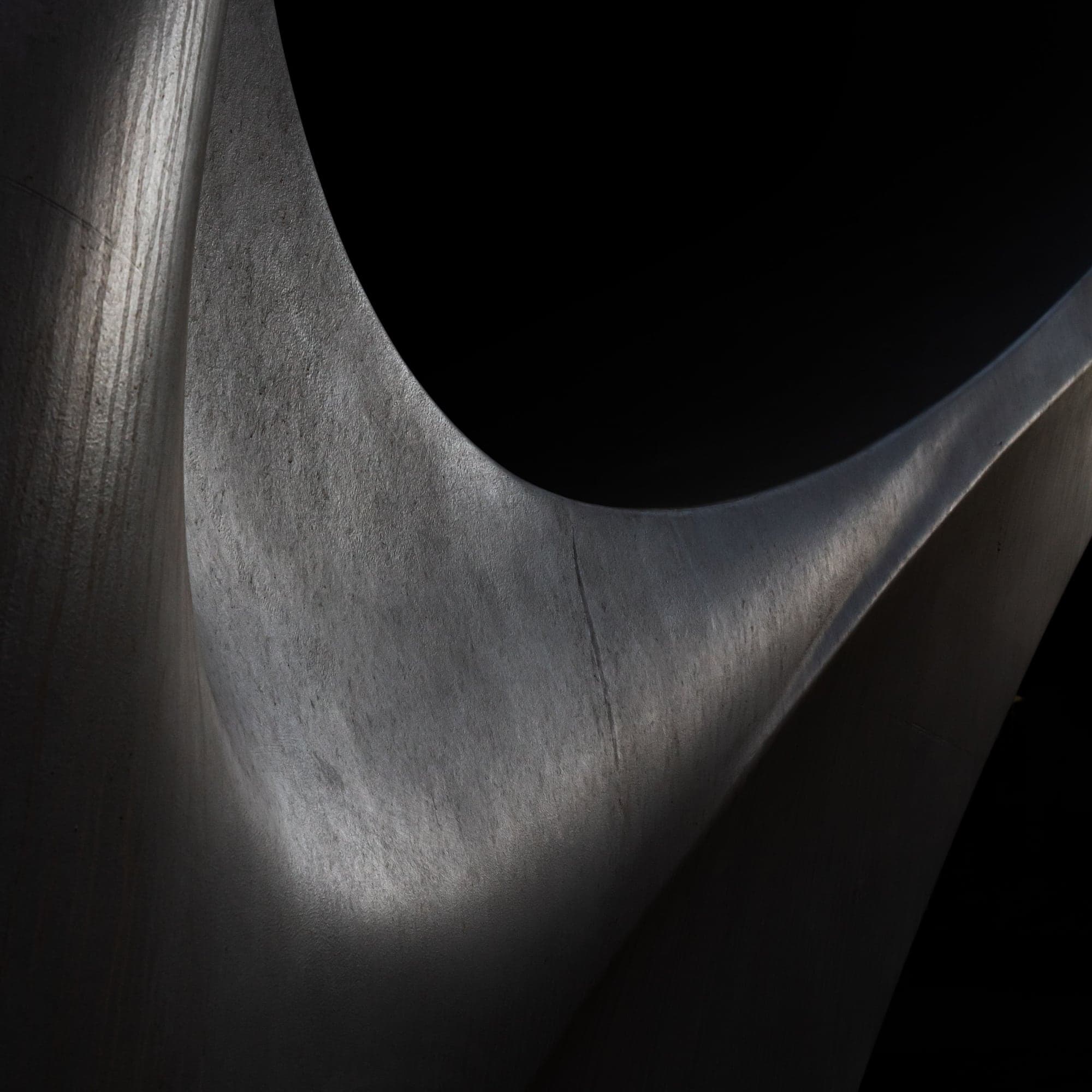 A sweeping curve of brushed grey metal catching soft light against a black background.