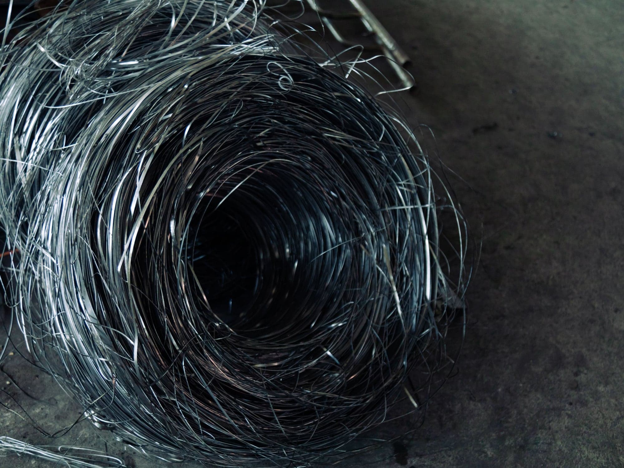 A tangled coil of bare metal wire lying on a concrete floor.